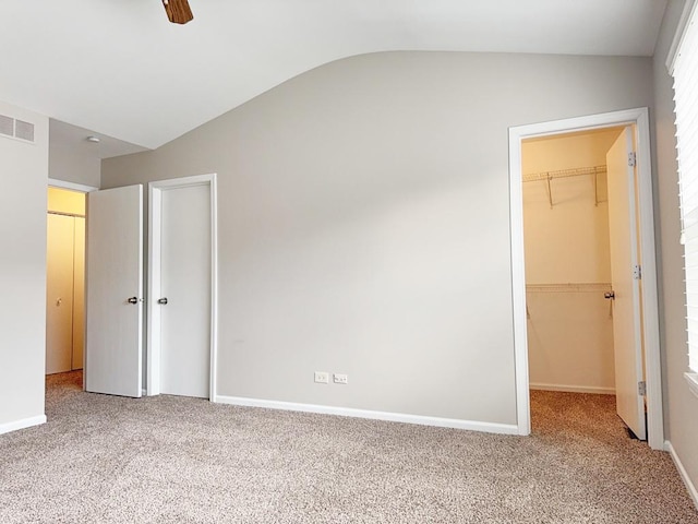 unfurnished bedroom featuring a spacious closet, ceiling fan, carpet floors, lofted ceiling, and a closet