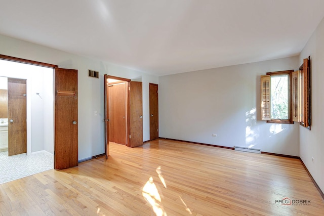 unfurnished bedroom featuring baseboard heating, ensuite bathroom, and light hardwood / wood-style flooring