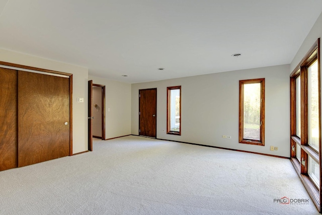 unfurnished bedroom featuring multiple windows, light carpet, and a closet