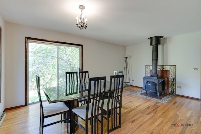 dining room with light wood-type flooring, an inviting chandelier, a wood stove, and baseboard heating