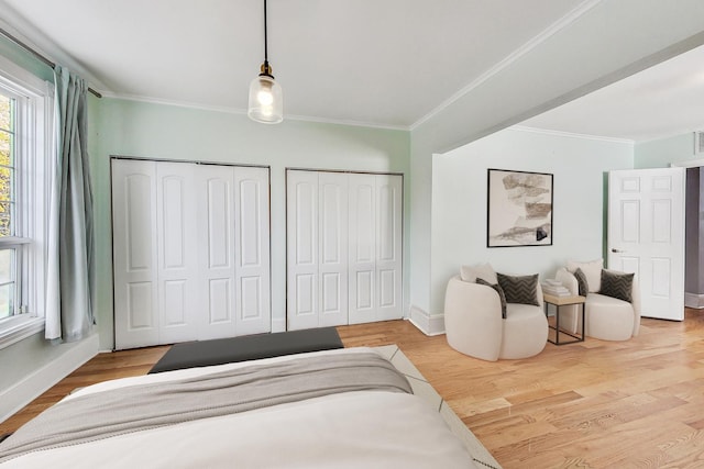 bedroom featuring ornamental molding, wood finished floors, two closets, and baseboards