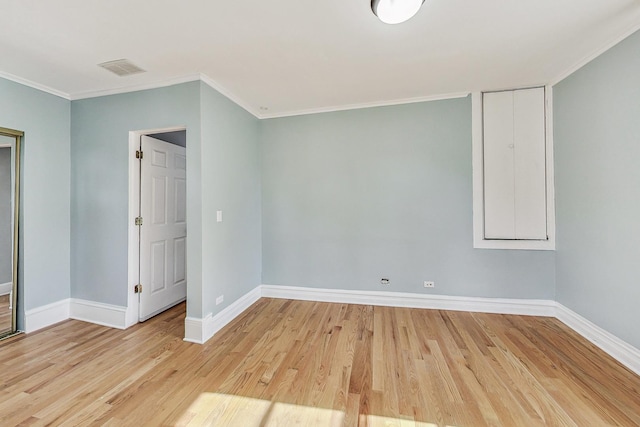 empty room featuring light wood-style floors, visible vents, ornamental molding, and baseboards