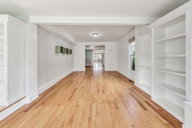 spare room featuring light wood finished floors, built in shelves, and baseboards