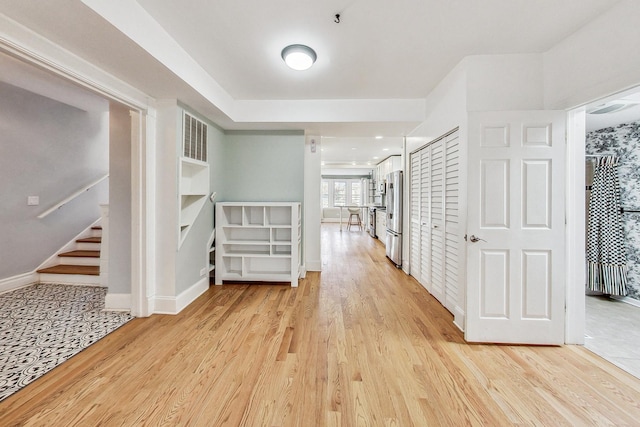 corridor with light wood-type flooring, baseboards, and stairs