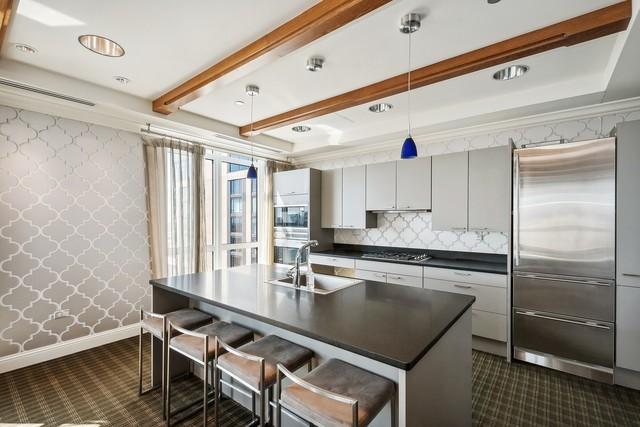 kitchen with wallpapered walls, dark countertops, a sink, stainless steel appliances, and beam ceiling