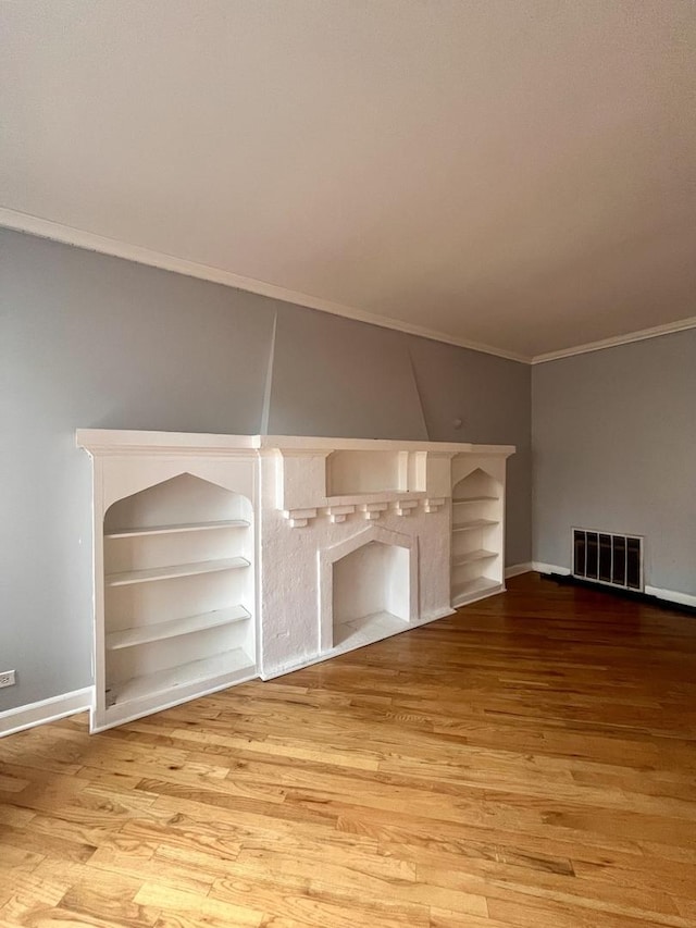 unfurnished living room featuring built in shelves, wood-type flooring, and crown molding