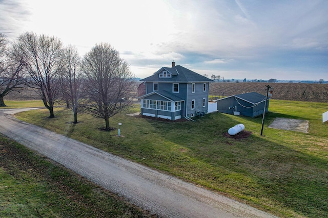 exterior space featuring a front yard, a rural view, an outdoor structure, and a sunroom