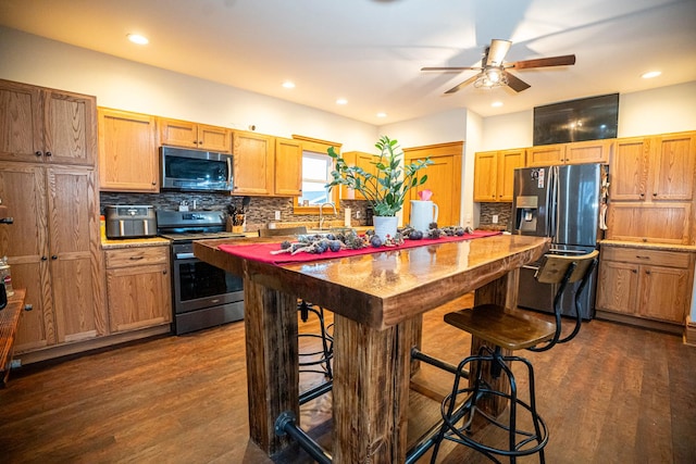 kitchen featuring ceiling fan, stainless steel appliances, a kitchen breakfast bar, dark hardwood / wood-style flooring, and decorative backsplash