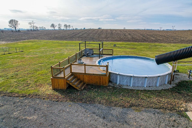 view of swimming pool with a lawn, a rural view, and a deck