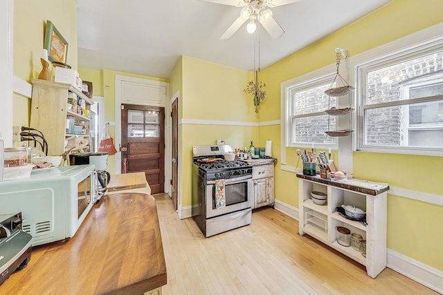 kitchen with hanging light fixtures, stainless steel gas range oven, ceiling fan, and light hardwood / wood-style flooring