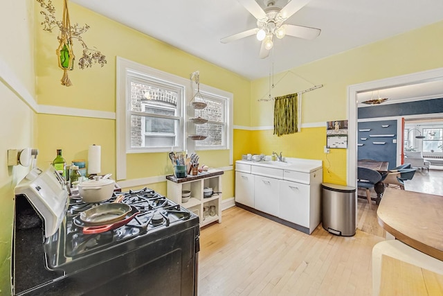 kitchen with sink, white cabinets, ceiling fan, gas range, and light hardwood / wood-style flooring