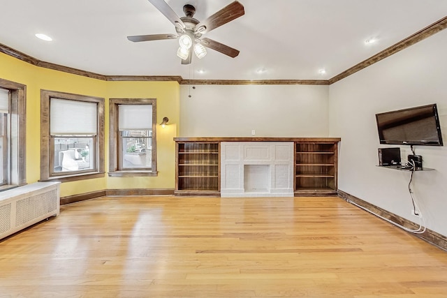 unfurnished living room featuring radiator, ceiling fan, a fireplace, ornamental molding, and light wood-type flooring