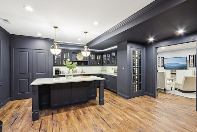 kitchen featuring decorative light fixtures, light wood-type flooring, ornamental molding, and a center island