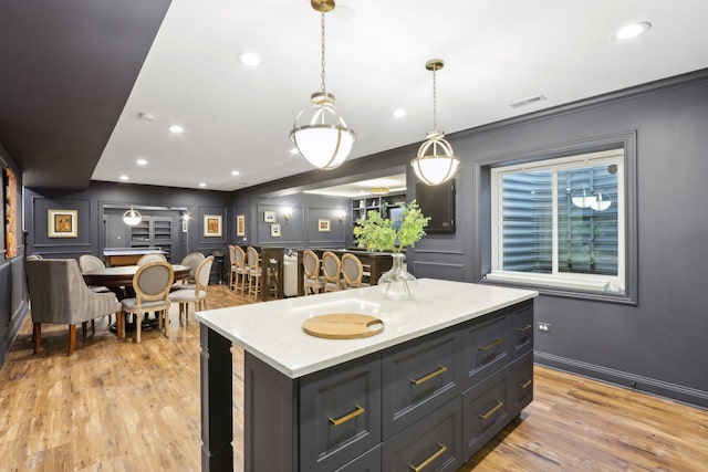 kitchen with light hardwood / wood-style floors, hanging light fixtures, crown molding, light stone counters, and a kitchen island