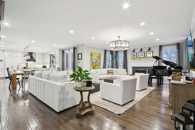 living room with dark wood-type flooring, a chandelier, crown molding, and a wealth of natural light