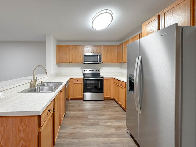 kitchen with kitchen peninsula, sink, light wood-type flooring, and appliances with stainless steel finishes