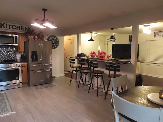 kitchen featuring hanging light fixtures, a kitchen breakfast bar, backsplash, appliances with stainless steel finishes, and hardwood / wood-style flooring