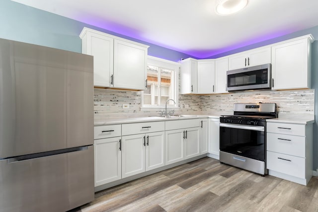 kitchen with appliances with stainless steel finishes, backsplash, light wood-type flooring, sink, and white cabinets