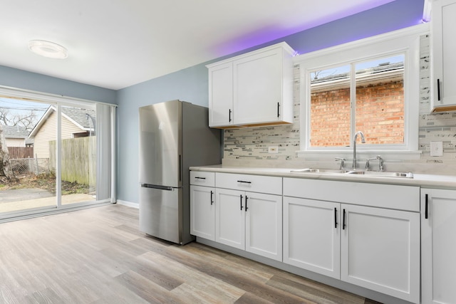 kitchen featuring light wood-type flooring, backsplash, sink, white cabinets, and stainless steel refrigerator