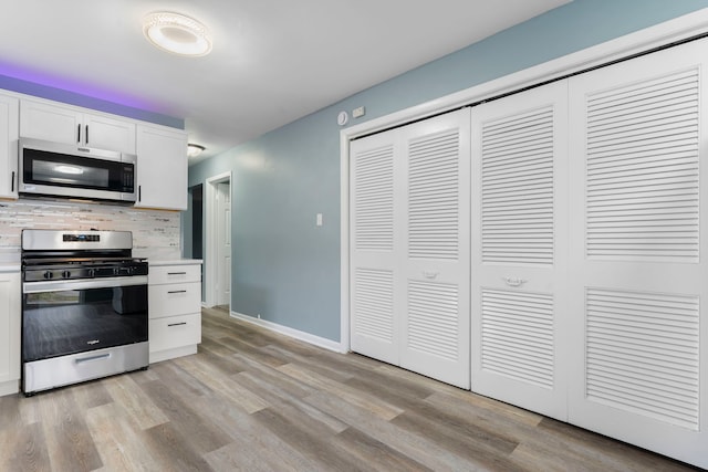 kitchen featuring tasteful backsplash, white cabinets, light wood-type flooring, and appliances with stainless steel finishes