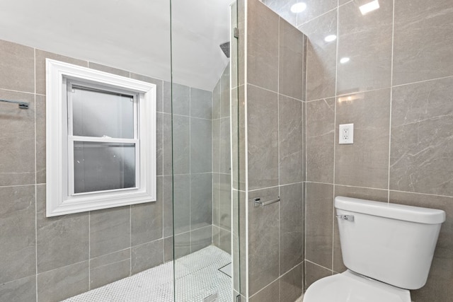 bathroom featuring tiled shower, toilet, and tile walls