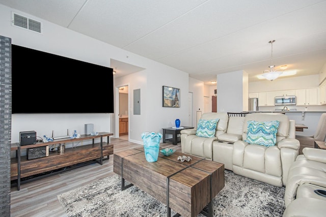 living room featuring a notable chandelier, light wood-type flooring, and electric panel