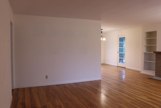 empty room with built in features, dark wood-type flooring, and an inviting chandelier