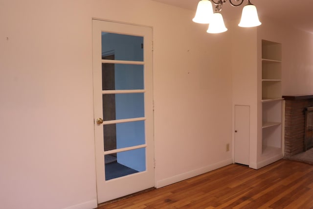 unfurnished room featuring built in features, wood-type flooring, and a notable chandelier