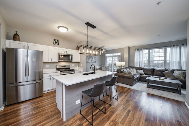 kitchen featuring white cabinetry, hanging light fixtures, stainless steel appliances, dark hardwood / wood-style flooring, and an island with sink