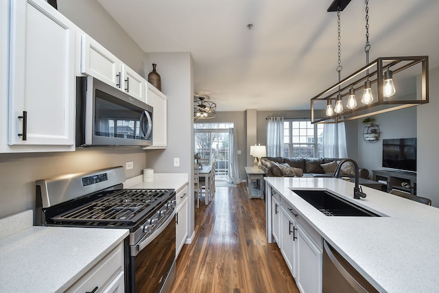 kitchen with hanging light fixtures, sink, light stone countertops, appliances with stainless steel finishes, and white cabinetry