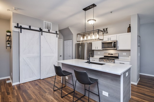 kitchen with pendant lighting, sink, a barn door, an island with sink, and stainless steel appliances