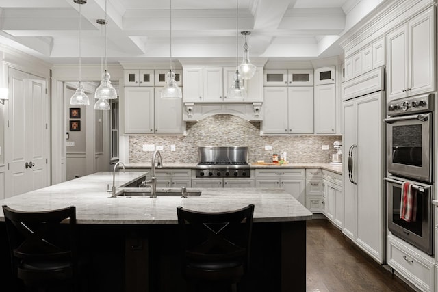 kitchen featuring a breakfast bar, a kitchen island with sink, coffered ceiling, sink, and double oven