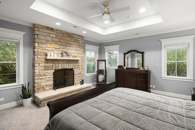 bedroom with a tray ceiling, a stone fireplace, ceiling fan, and crown molding