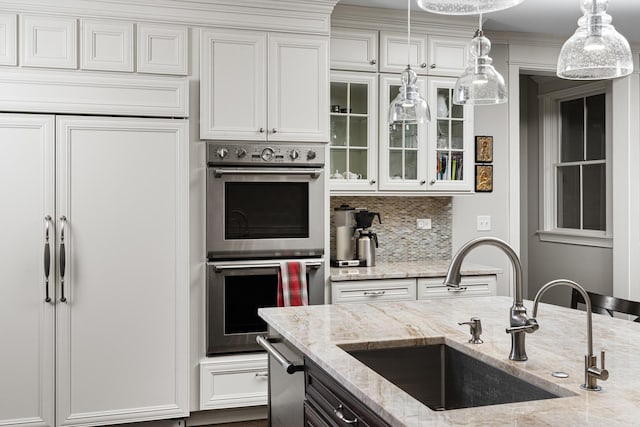 kitchen featuring white cabinets, light stone countertops, stainless steel double oven, and sink