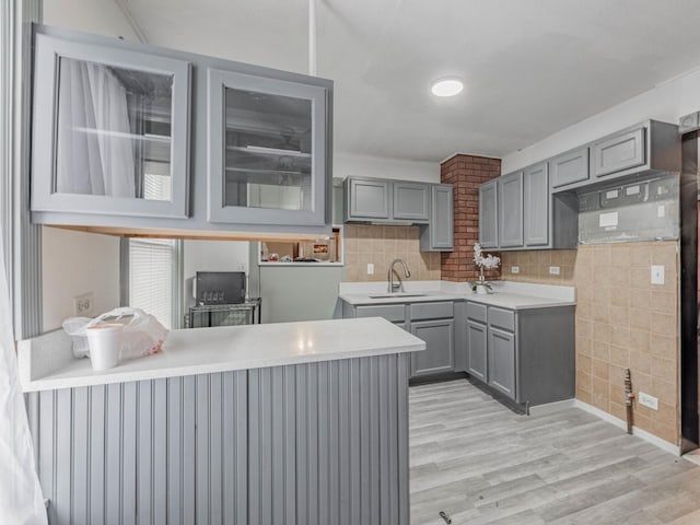 kitchen with gray cabinetry, sink, light hardwood / wood-style flooring, backsplash, and kitchen peninsula