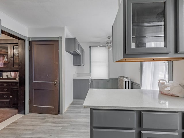 kitchen with kitchen peninsula, light stone countertops, light wood-type flooring, gray cabinetry, and ceiling fan