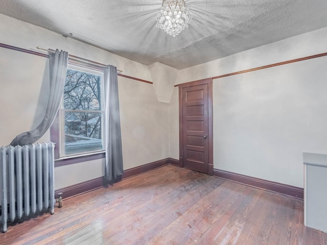 unfurnished room with hardwood / wood-style flooring, radiator heating unit, a textured ceiling, and an inviting chandelier