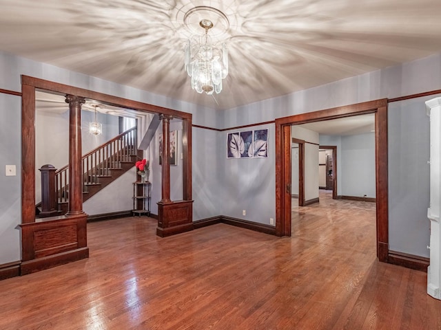 unfurnished living room featuring hardwood / wood-style floors, a notable chandelier, and ornate columns