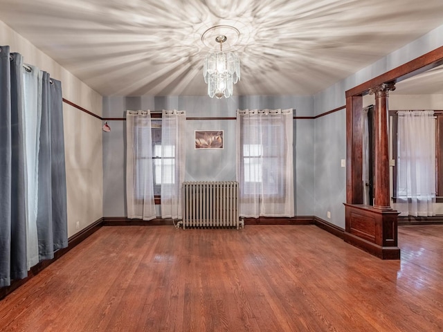 empty room with a chandelier, wood-type flooring, radiator heating unit, and ornate columns