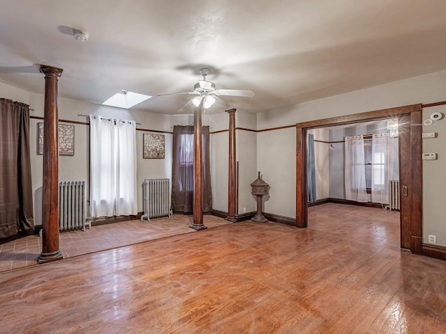 empty room with radiator, ceiling fan, a skylight, and ornate columns