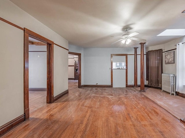 spare room featuring decorative columns, ceiling fan, radiator heating unit, and light wood-type flooring