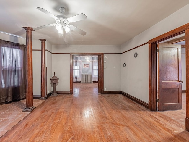 empty room featuring decorative columns, radiator, light hardwood / wood-style floors, and ceiling fan