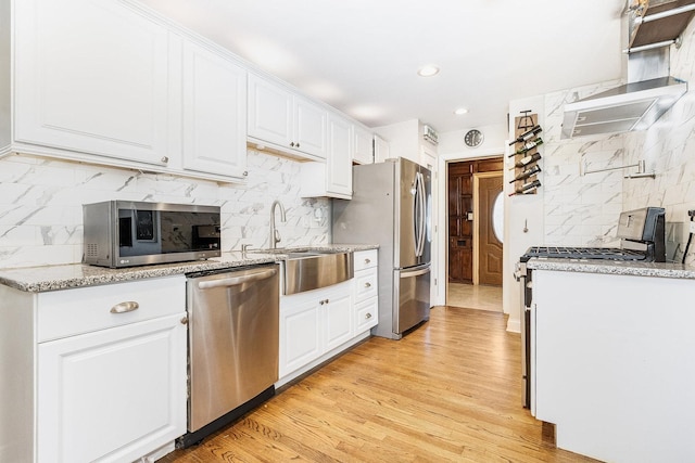 kitchen featuring white cabinetry, stainless steel appliances, light stone counters, light hardwood / wood-style flooring, and decorative backsplash