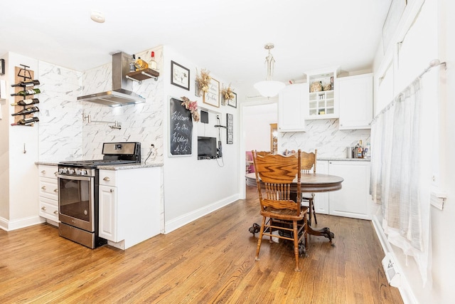 kitchen featuring gas range, wall chimney range hood, backsplash, white cabinets, and light wood-type flooring