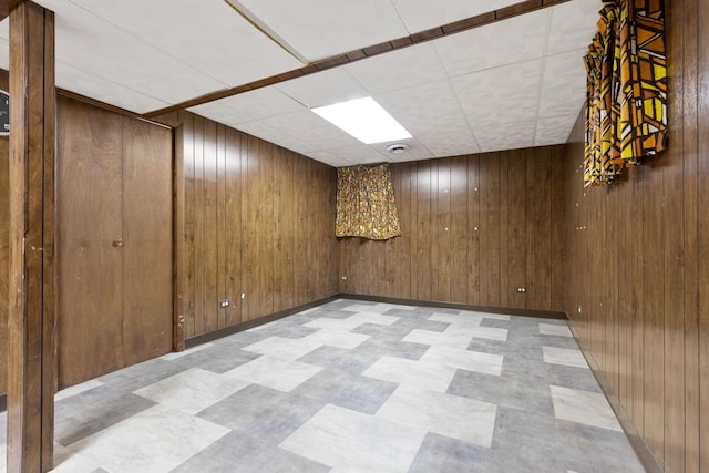 basement with a drop ceiling and wood walls