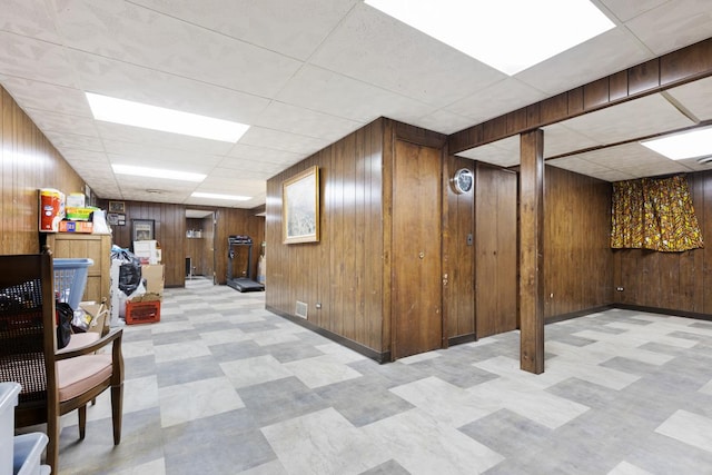 basement featuring a drop ceiling and wooden walls