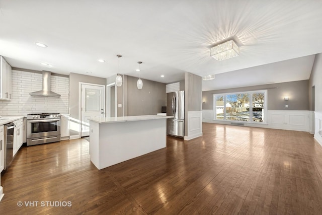 kitchen featuring wall chimney exhaust hood, appliances with stainless steel finishes, decorative light fixtures, and white cabinets