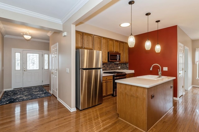 kitchen featuring appliances with stainless steel finishes, decorative light fixtures, an island with sink, sink, and light hardwood / wood-style flooring