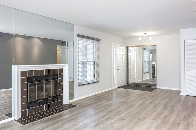 unfurnished living room featuring a tile fireplace, an inviting chandelier, and hardwood / wood-style flooring