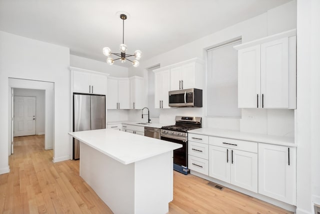 kitchen with appliances with stainless steel finishes, light hardwood / wood-style floors, white cabinets, a kitchen island, and decorative light fixtures